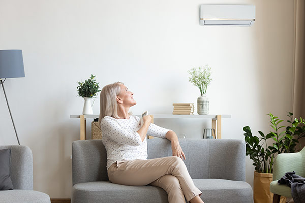 Woman operating an air conditioner with a remote from her couch